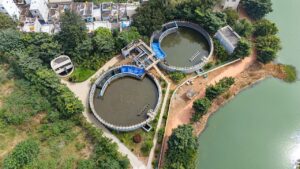 Vista aérea de uma estação de tratamento de esgoto com tanques circulares ao lado de um lago urbano