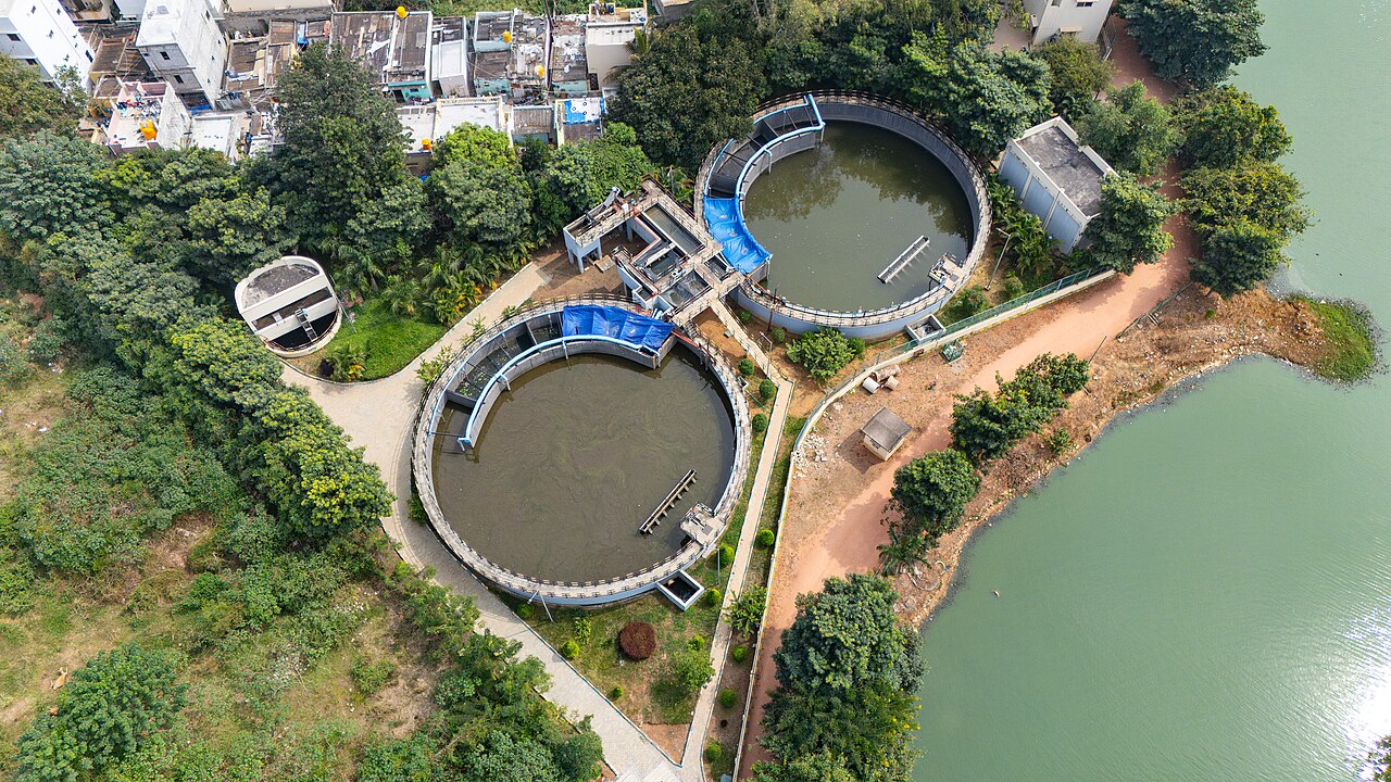 Vista aérea de uma estação de tratamento de esgoto com tanques circulares ao lado de um lago urbano